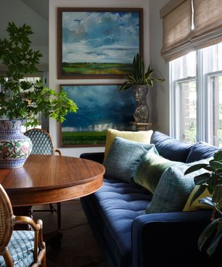 dining nook with navy seating, round wooden table, two landscape artworks