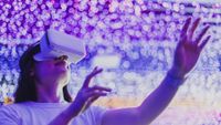 A woman wearing a VR headset with dramatic, colourful lighting across the background