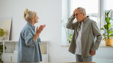 An older couple face each other at home, looking overwhelmed.