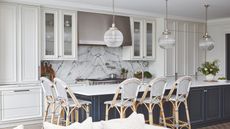 A kitchen with white shaker cabinetry with glass-fronted cabinets, a large navy blue island with a white countertop, and a book-matched marble backsplash