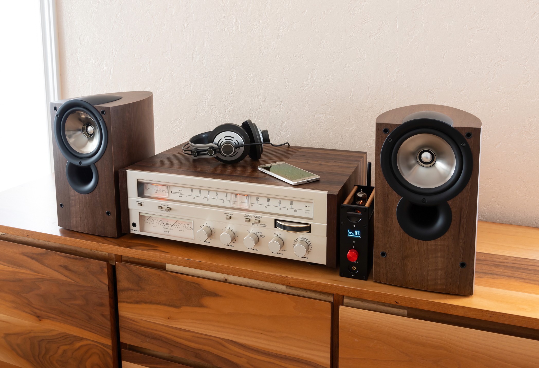 Home Vintage Stereo Receiver with Loudspeakers and Headphones Placed on Wooden Retro Shelf. Smartphone as a Source, New and Old Technology Working Together.