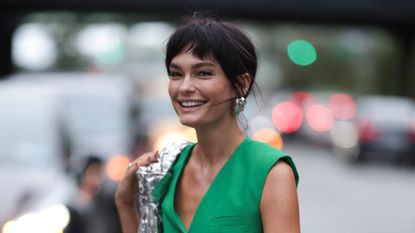 Quigley Goode wearing green waistcoat, silver bag and earrings and the best eyeshadow stick look