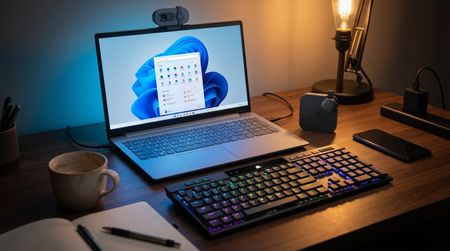 A laptop, keyboard, and webcam on a desk in a home office 
