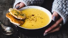 3/4 shot of a bowl of yellow soup with hands gently holding the bowl 