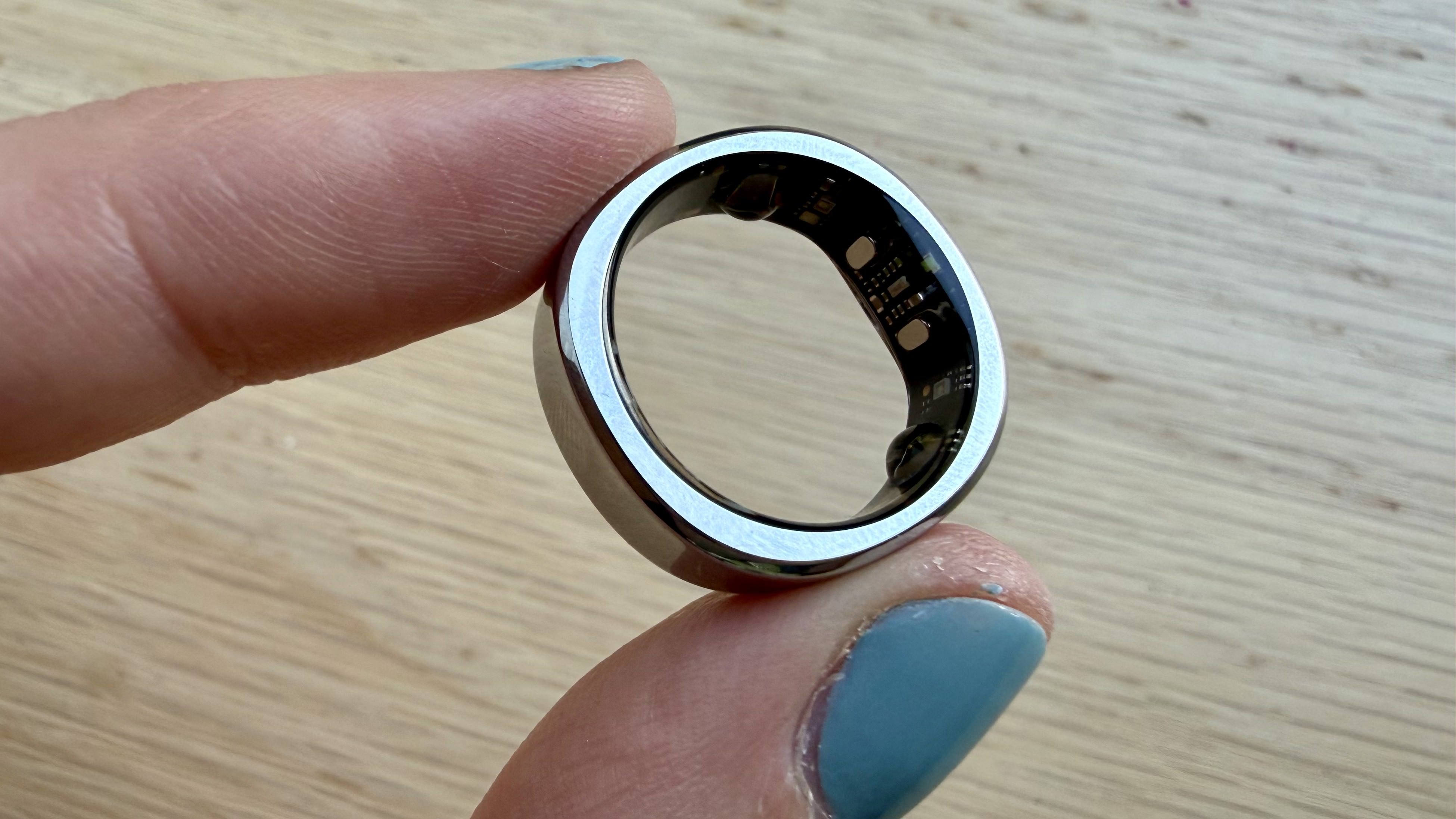 Becca holding the RingConn Gen 3 smart ring in silver above a wooden surface