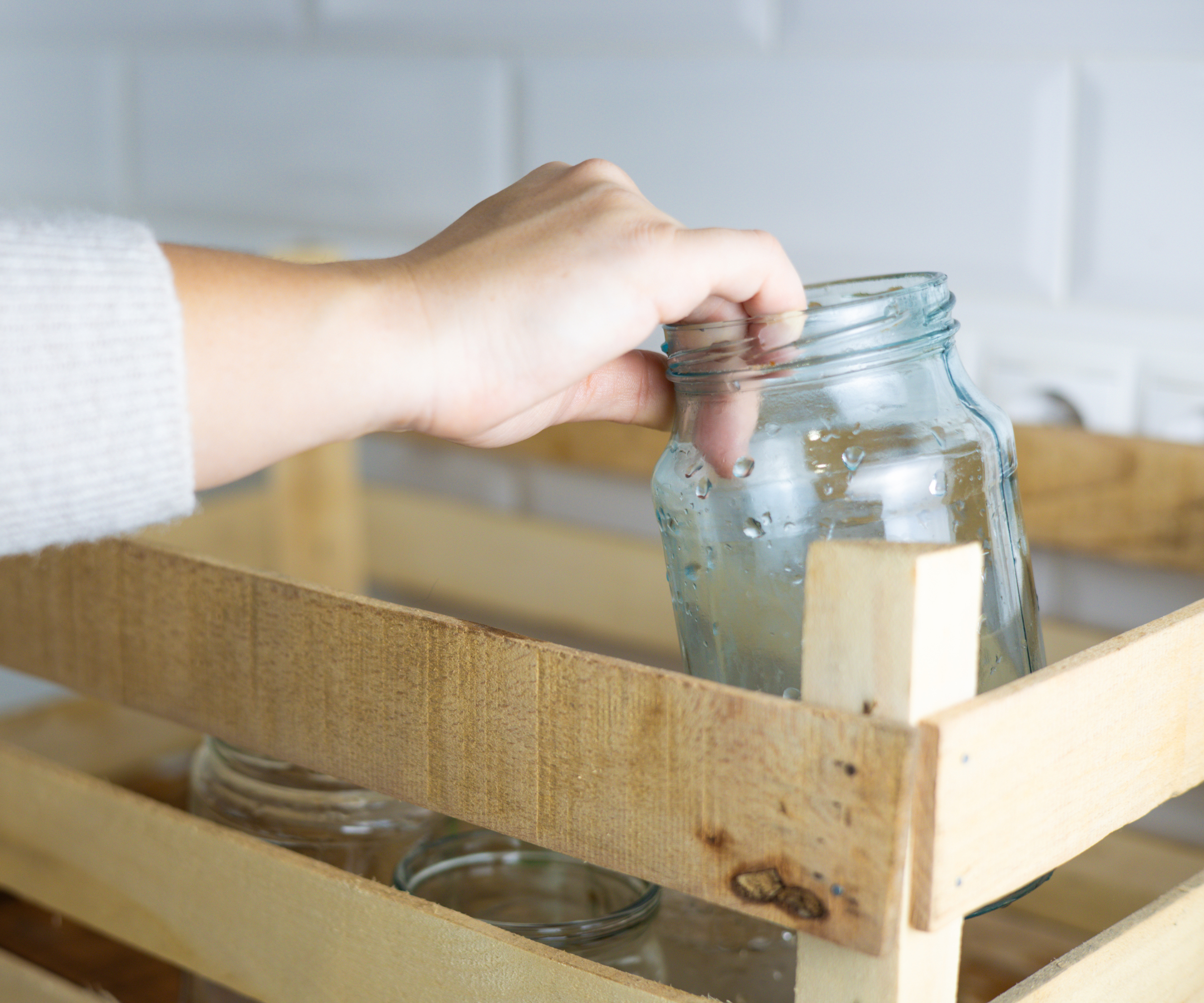 Hand placing a clean jar into a wooden crate