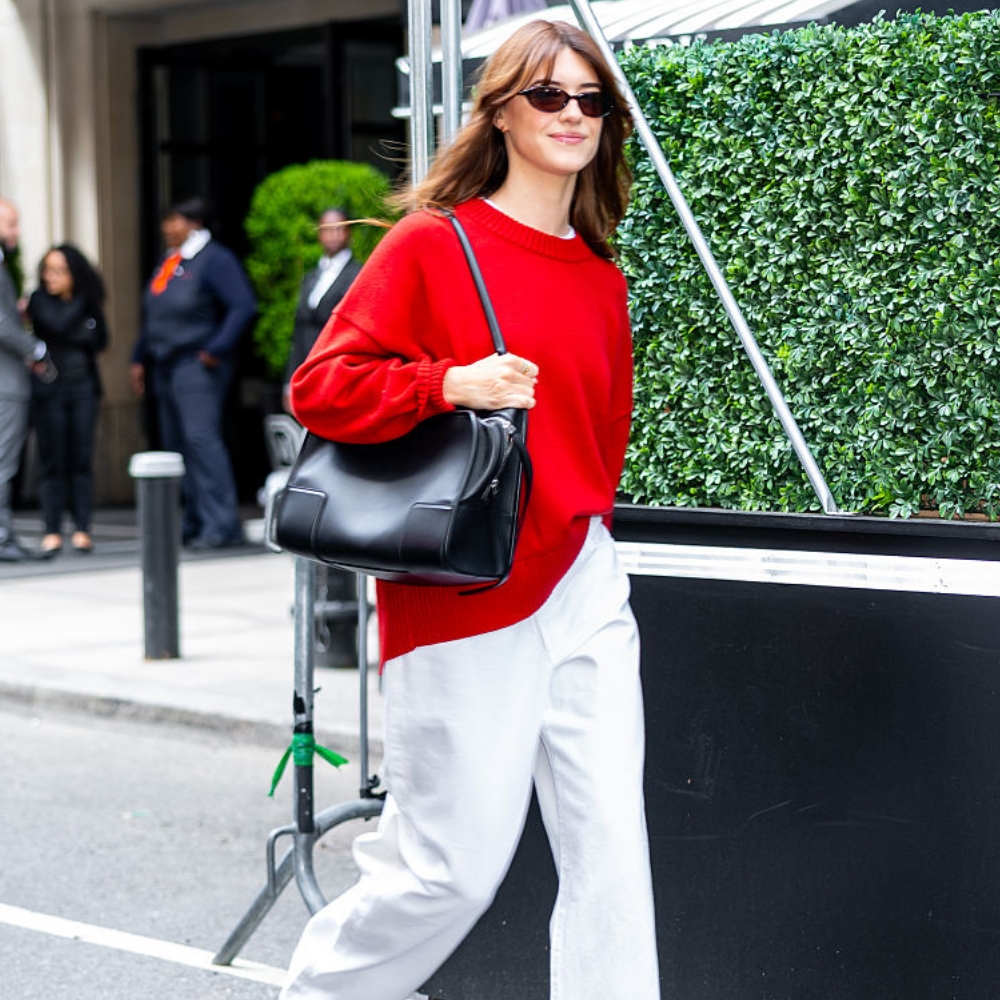 daisy edgar jones wears a red jumper, white jeans, and a black leather bag
