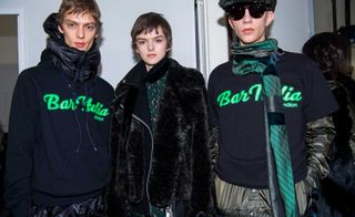 Group of models posing for the picture in black clothing with green text embroidery