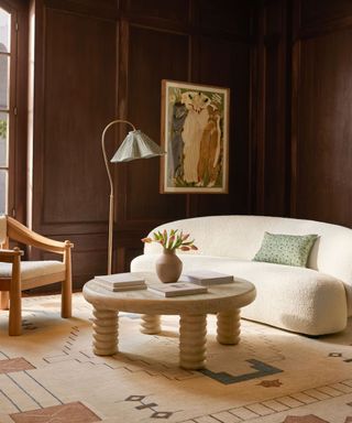 a dark wooden panelled living room with a small curved sofa made from boucle and a contemporary coffee table and rug