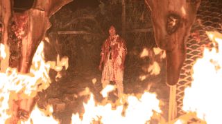 Dr. Lim wearing bloody lab coat standing in front of a large fire in Sweet Home