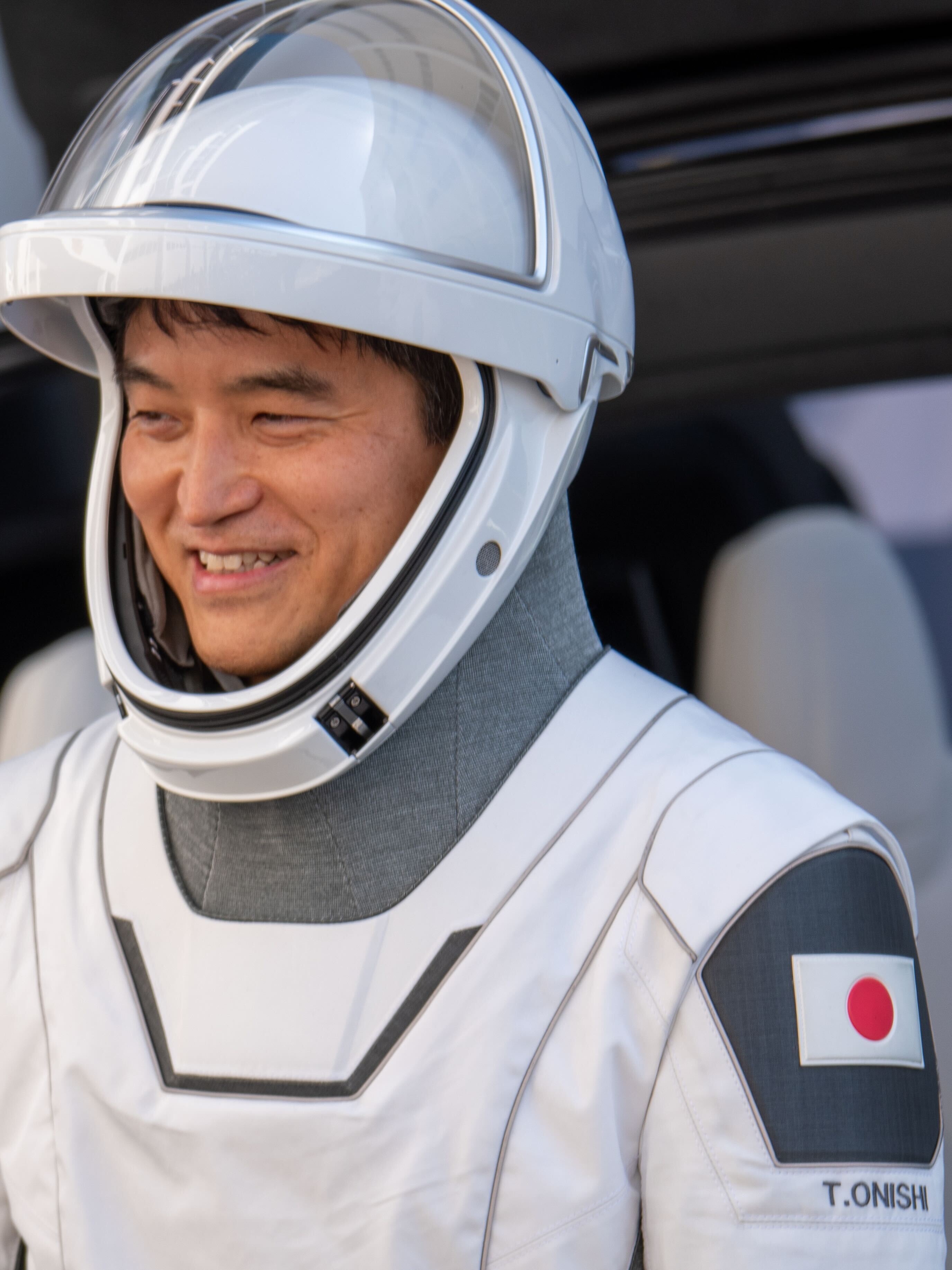 astronauts walk out of a building and board black cars.