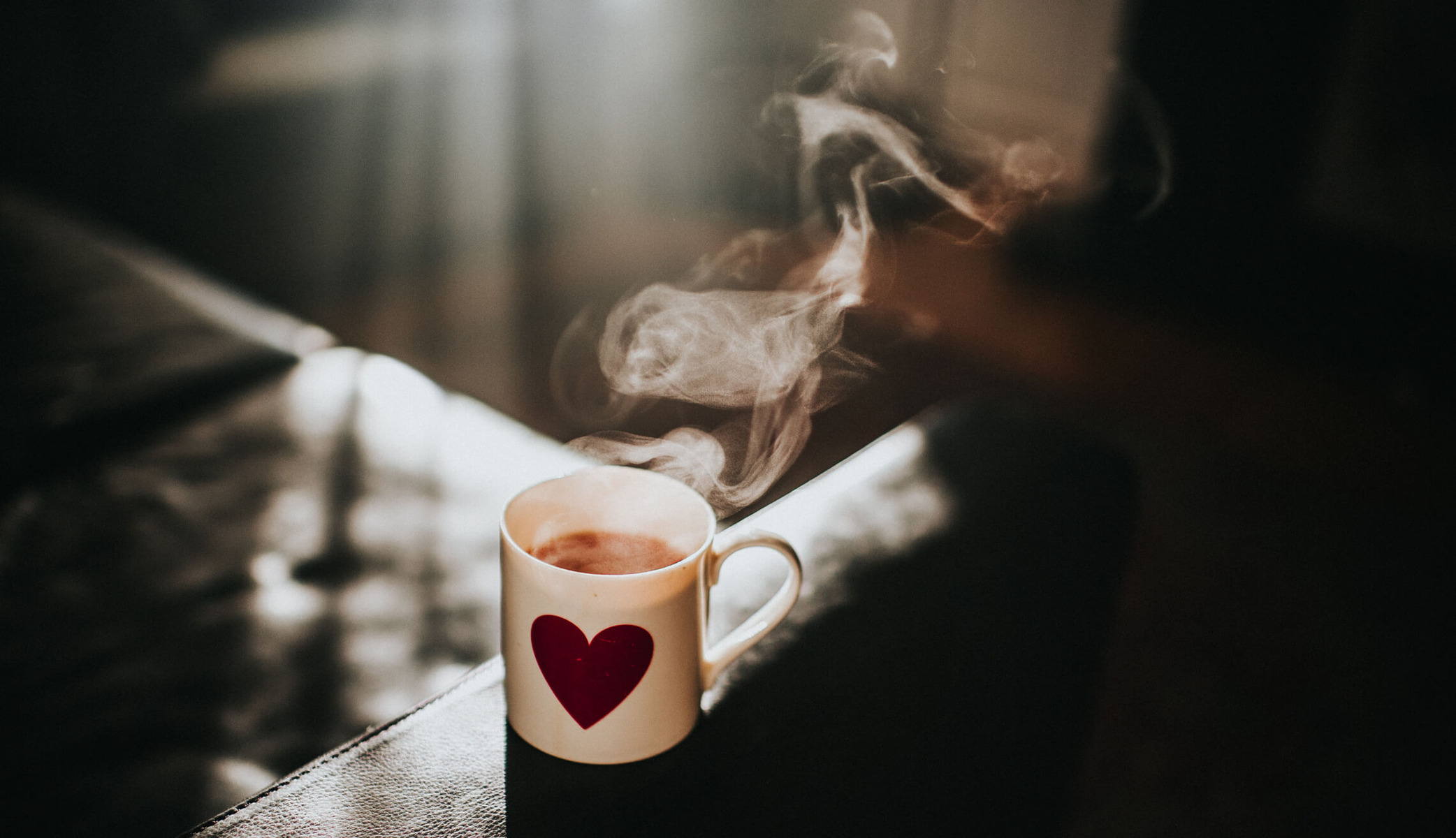 A white mug with a red heart contains steaming hot tea 