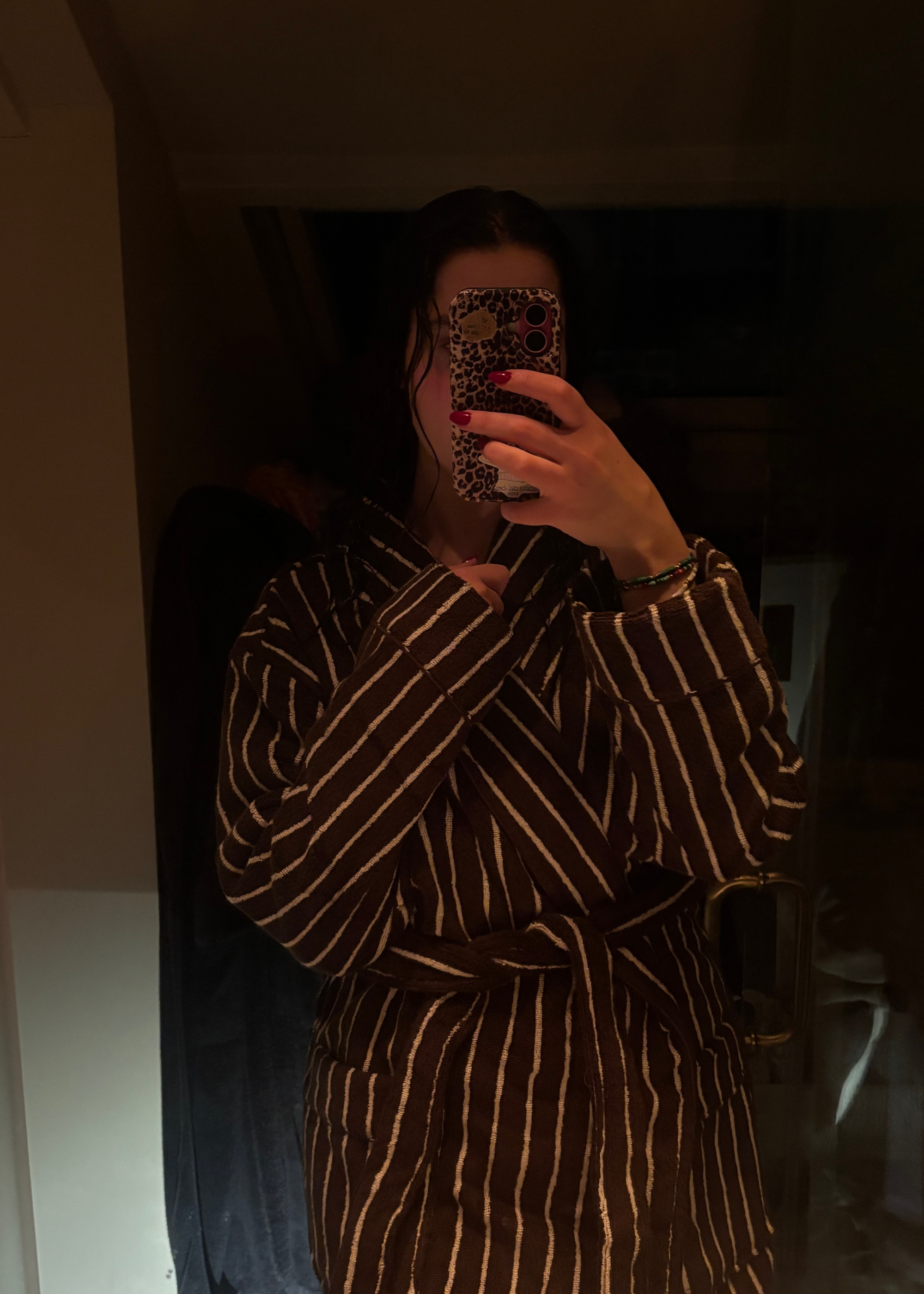 A woman wearing a striped black and white bathrobe taking a mirror selfie.