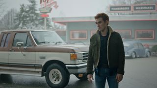 KJ Apa as Archie Andrews stands in front of a car in Riverdale.