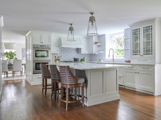 white kitchen with wooden flooring and brown bar style seating under a white island in the rooms center