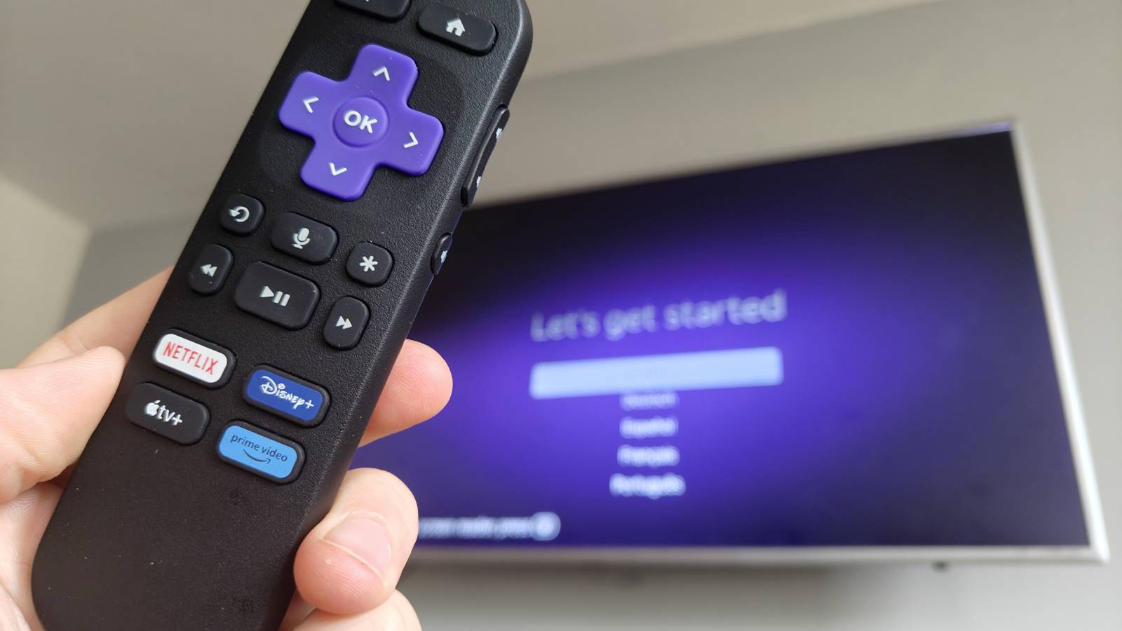 The Roku Streaming Stick&#039;s remote in front of a screen saying &quot;Let&#039;s get started&quot;