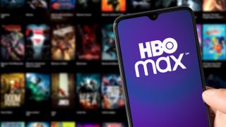 The HBO Max logo on a phone in front of a screen of posters