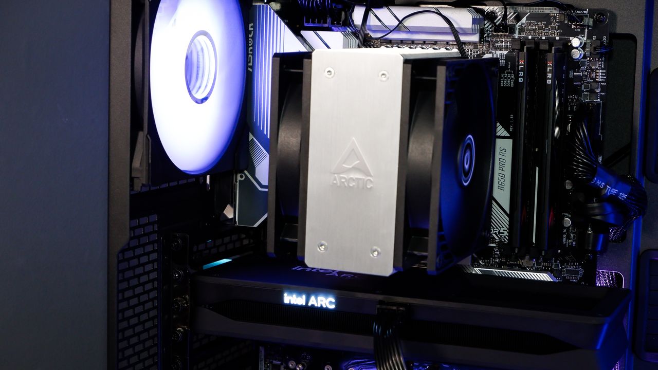 A gaming PC sat on a desk with purple RGB lighting on the fans and light bar enabled.