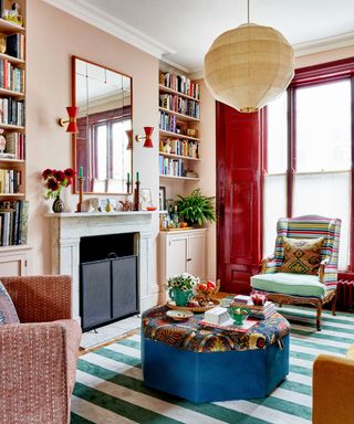 a pink and red living room with a green striped rug and blue ottoman