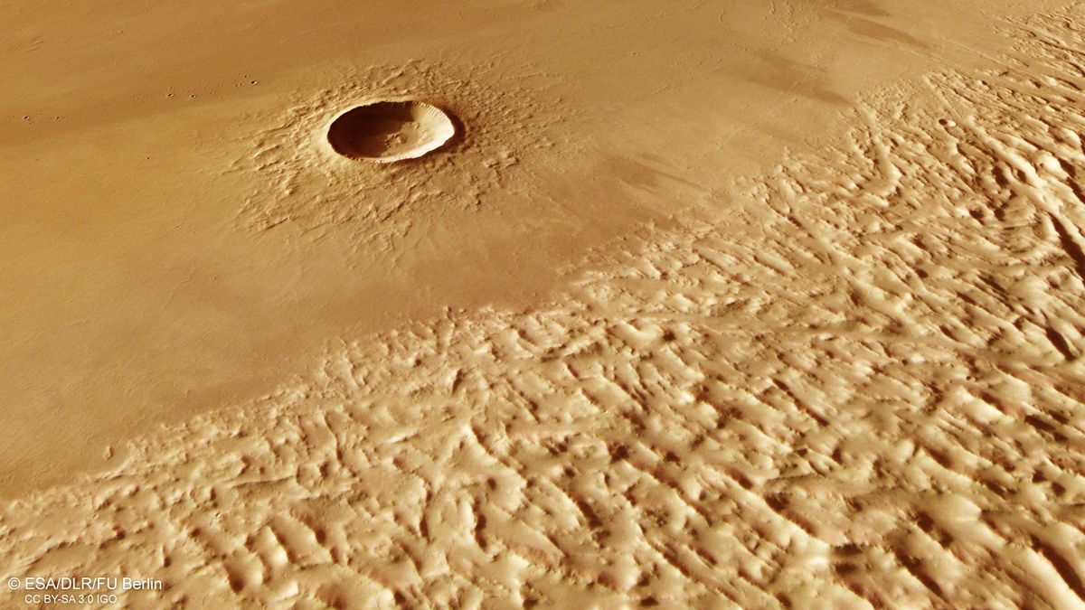 A view of sandy-colored striations on Mars&#039; surface. Toward the top left looks to be a deep crater.