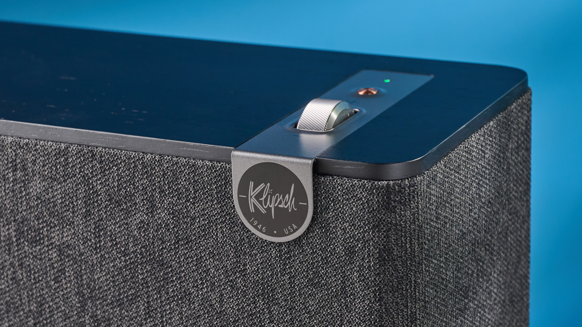 Klipsch The One Plus Bluetooth speaker in matte black photographed in front of a blue background.