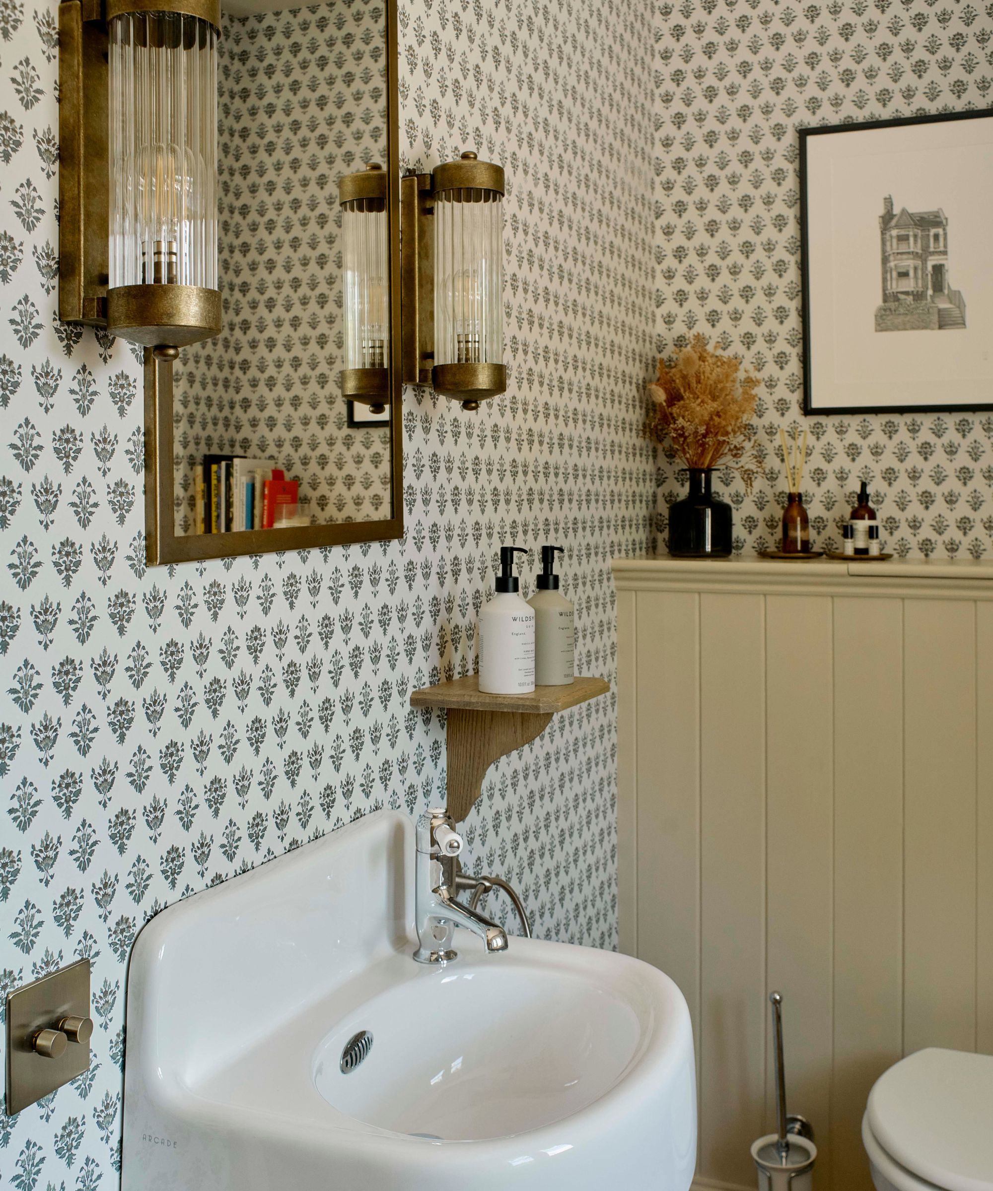 small vintage style powder room with butter yellow panelling and a block print small motif wallpaper with brass mirror and sconces