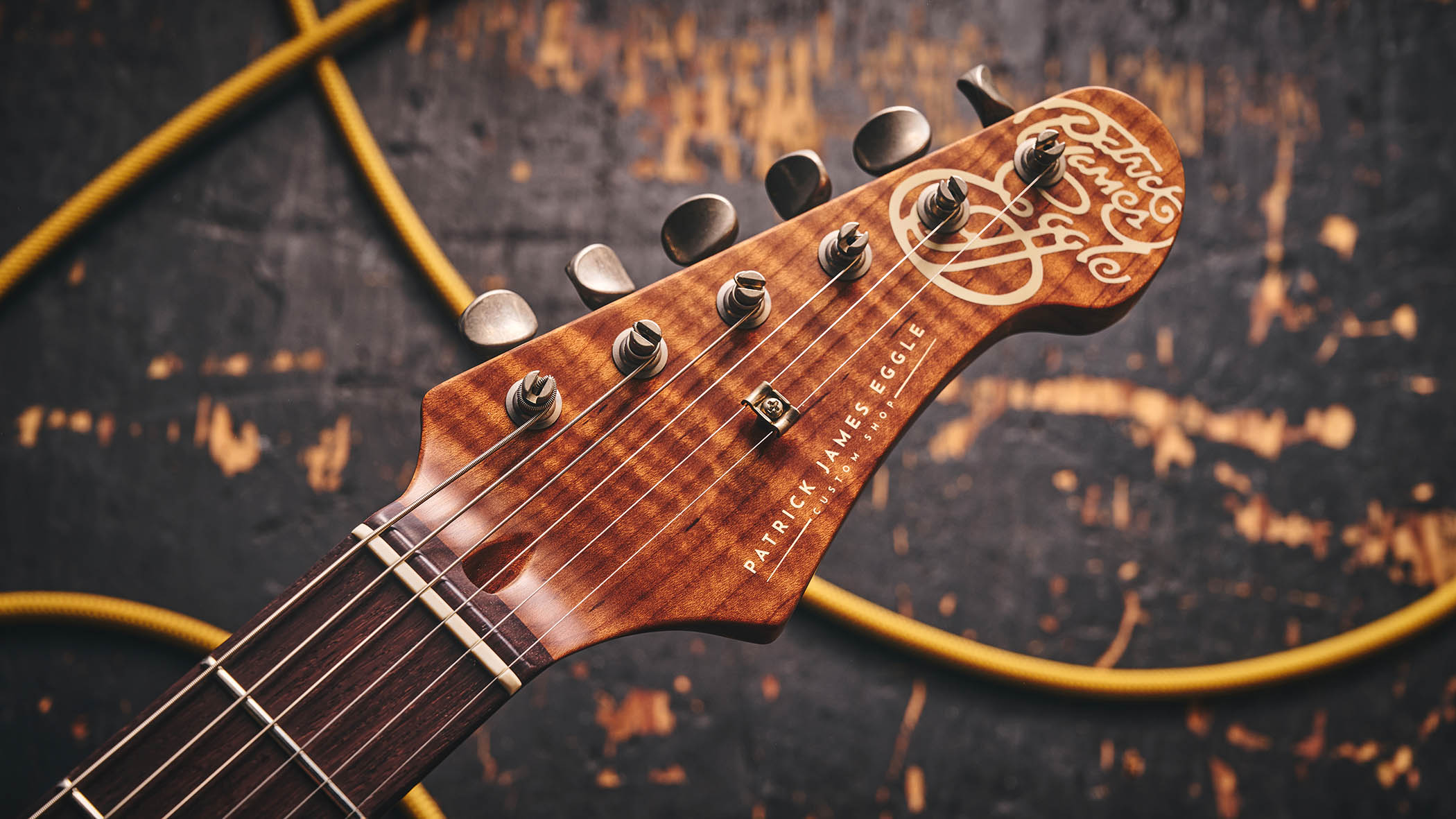 Patrick James Eggle Oz-t Cabronita Thinline; this semi-hollow T-style has a dark sunburst that reveals all the open grain, complementing the tortoiseshell pickguard, and is photographed here against a distressed floor, white and wooden backgrounds.