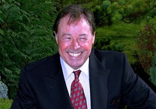 Bill Treacher smiling wearing a suit and red tie with a white shirt