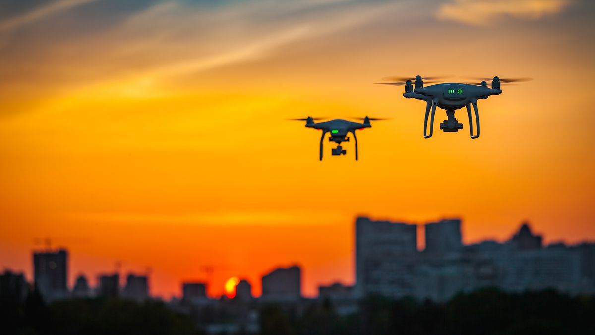 Two drones flying over a cityscape while the sun sets