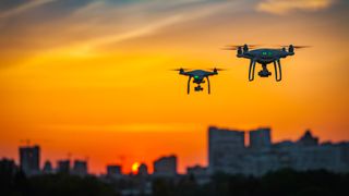 Two drones flying over a cityscape while the sun sets