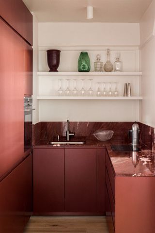 A small kitchen with deep red handleless cabinets, deep red marble countertop and white walls and open shelving