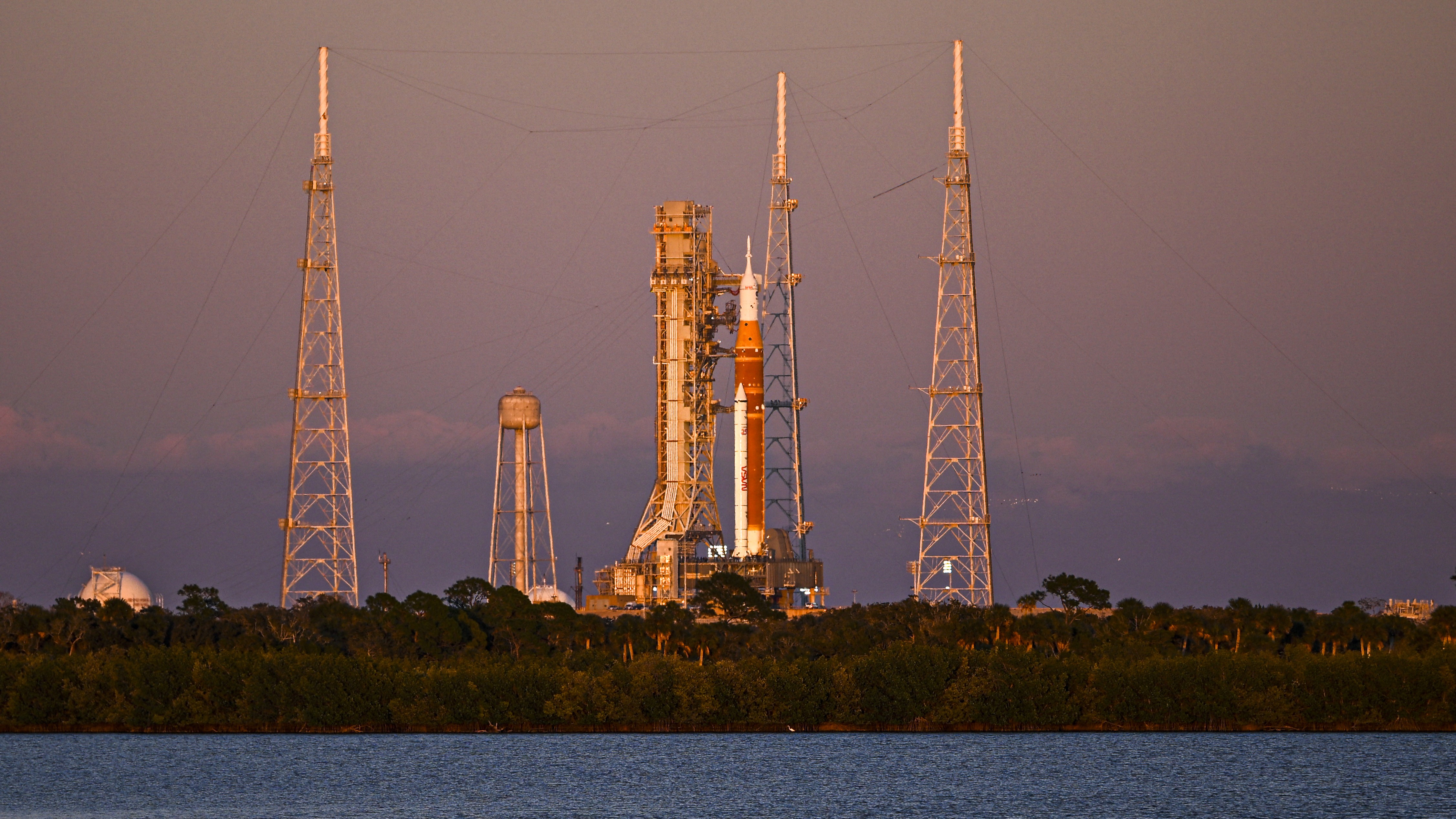 A photo of the Artemis II rocket sitting on a launchpad at Kennedy Space Center in Cape Canaveral, Florida, at sunset. 