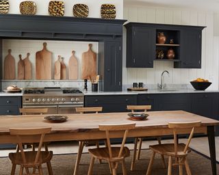Dark grey kitchen with wooden table and chairs and a selection of wooden chopping boards on display.