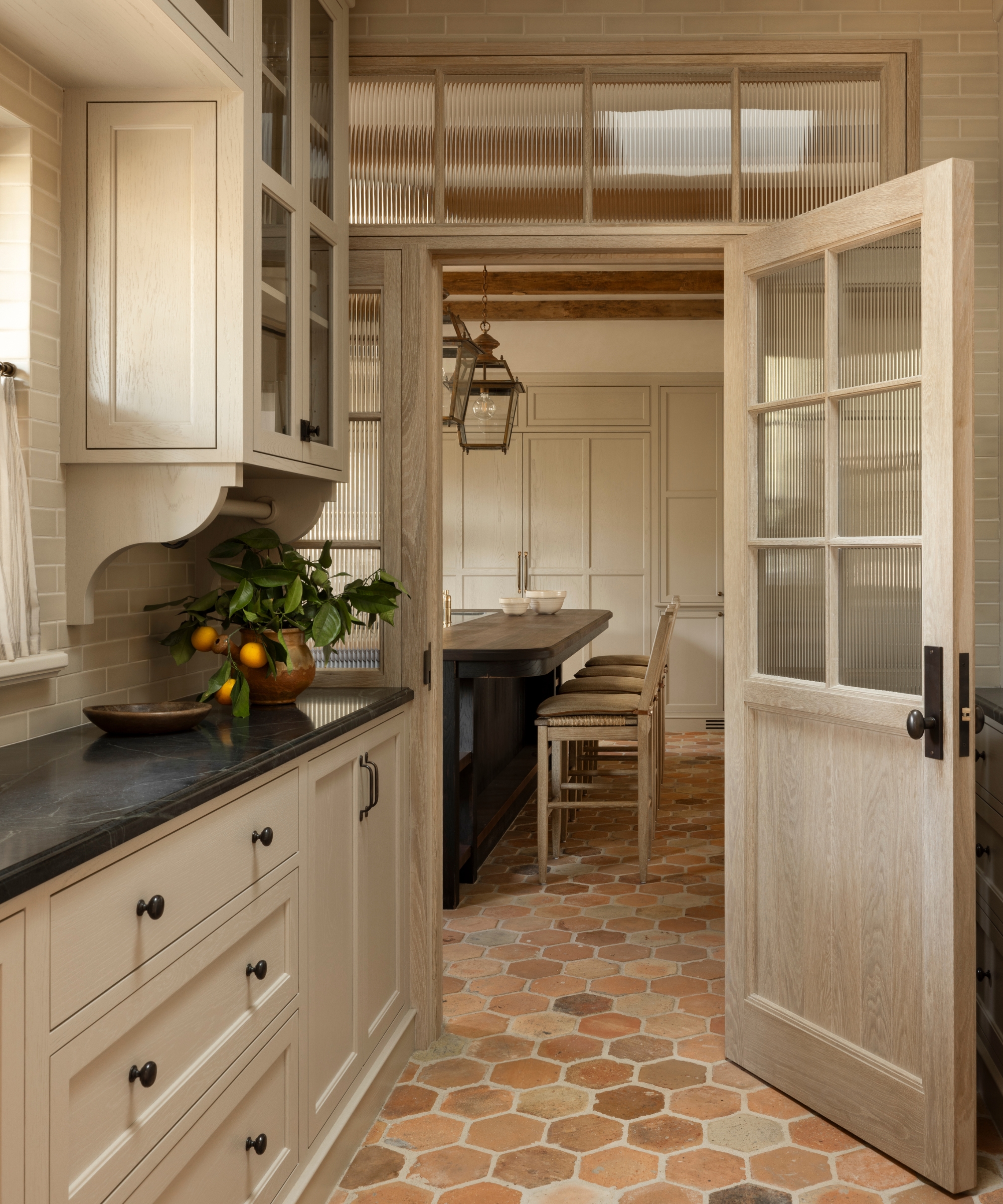 a war white kitchen with black countertops and hexagonal terracotta floor tiles