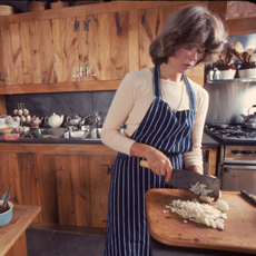 American media mogul and businesswoman Martha Stewart uses a cleaver to chop root vegetables in a well-stocked kitchen, August 1976