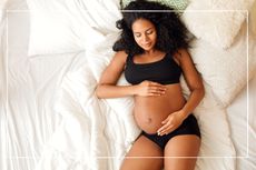 Woman lying on a bed cradling her pregnant belly