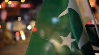 The Pakistan flag in front of a blurred city backdrop