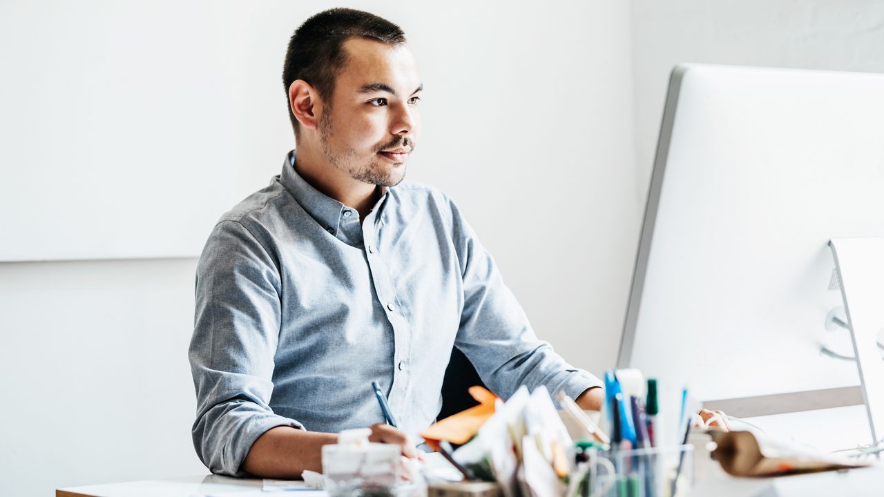 A young man sits at a desk in an office and works on a computer.