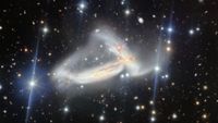 A dark scene with glowing dots on top of it. In the center, there are two wispy galaxies that look tangled in one another.