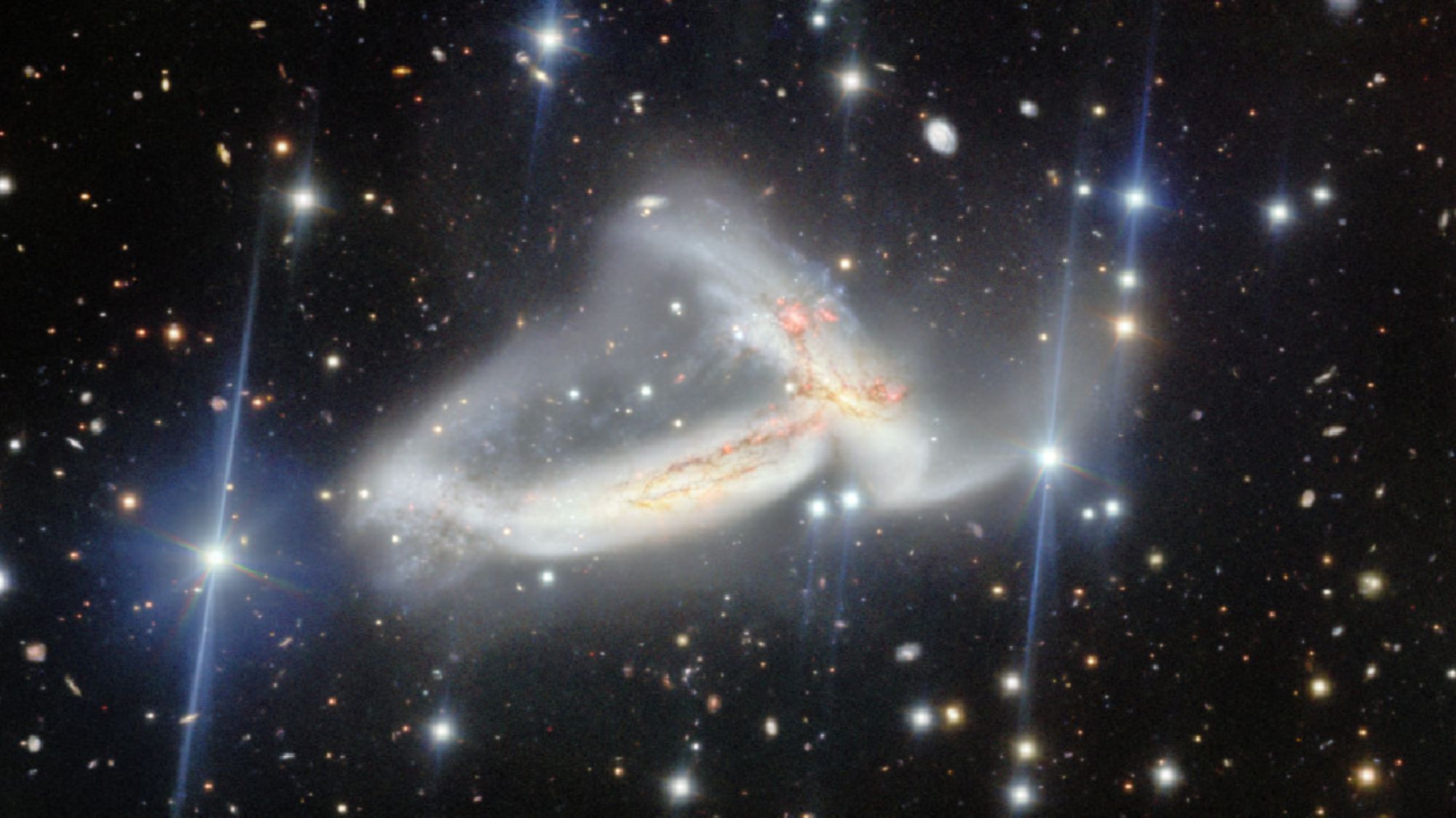 A dark scene with glowing dots on top of it. In the center, there are two wispy galaxies that look tangled in one another.