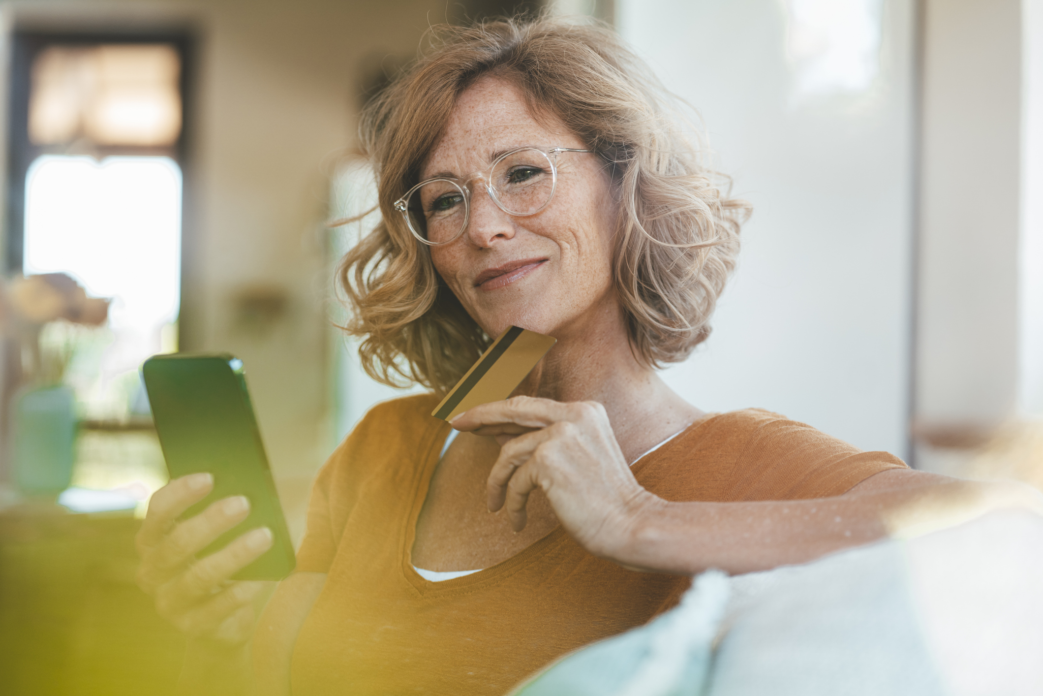 Smiling woman with credit card using smart phone at home