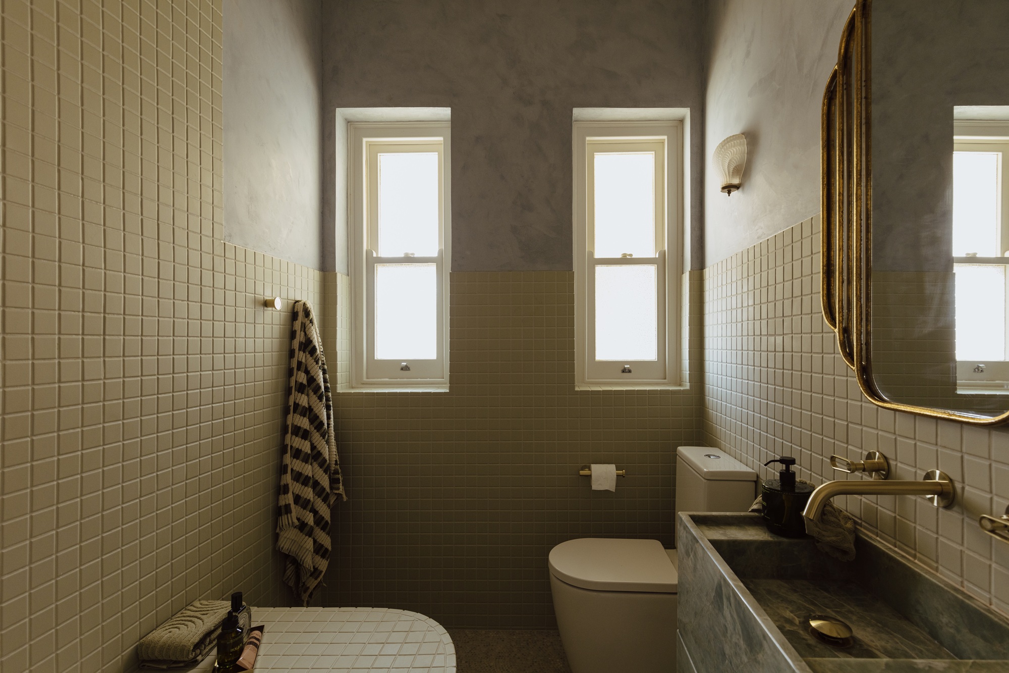 a modern art deco bathroom with a stacked mirror brass finishes and yellow tiles