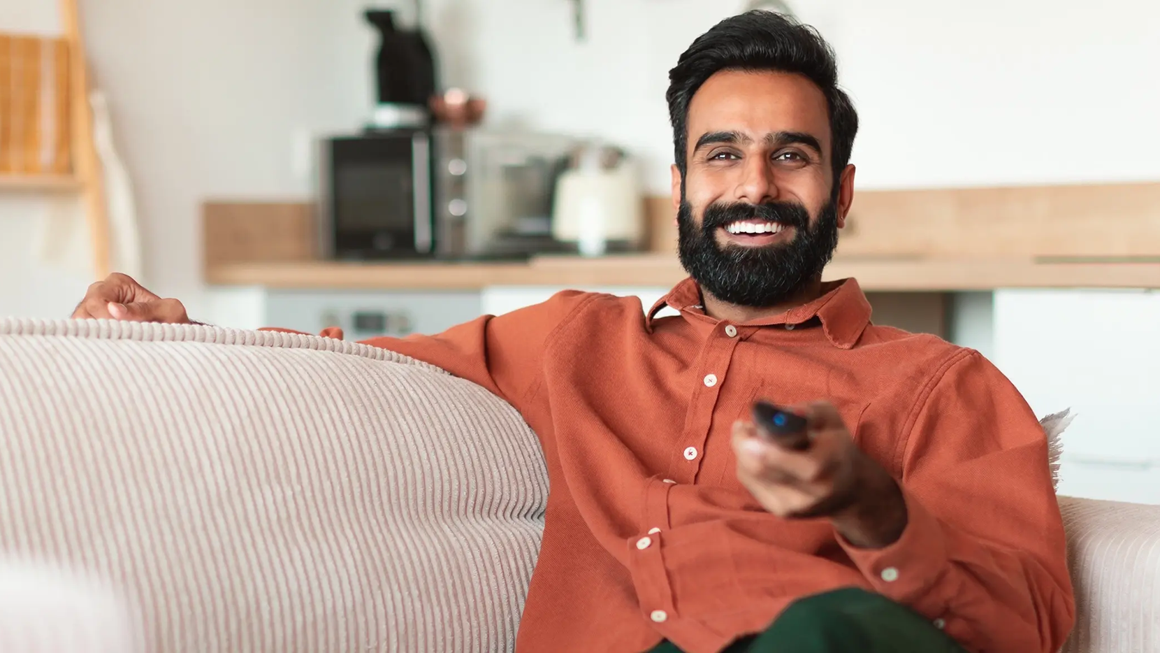 Smiling man holding a remote on a couch