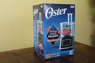 The Oster 10-Cup Food Processor with Easy-Touch in its cardboard box
