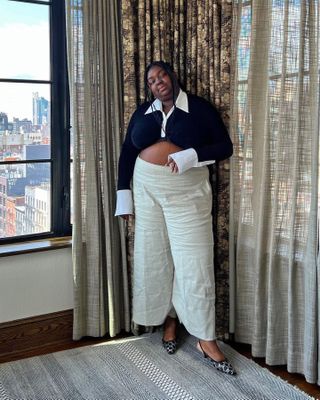 British fashion influencer Abisola Omole poses in a hotel room wearing a collared long sleeve top, neutral linen pants, and Gucci logo-print slingback kitten heels.