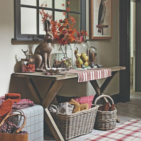 An autumn-decorated hallway with a rustic console table adorned with a glass vase of autumn foliage and mini pumpkins displayed under a cake dome