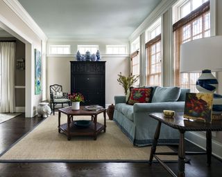 A living room with tall windows, blue sofa and black wooden secretary