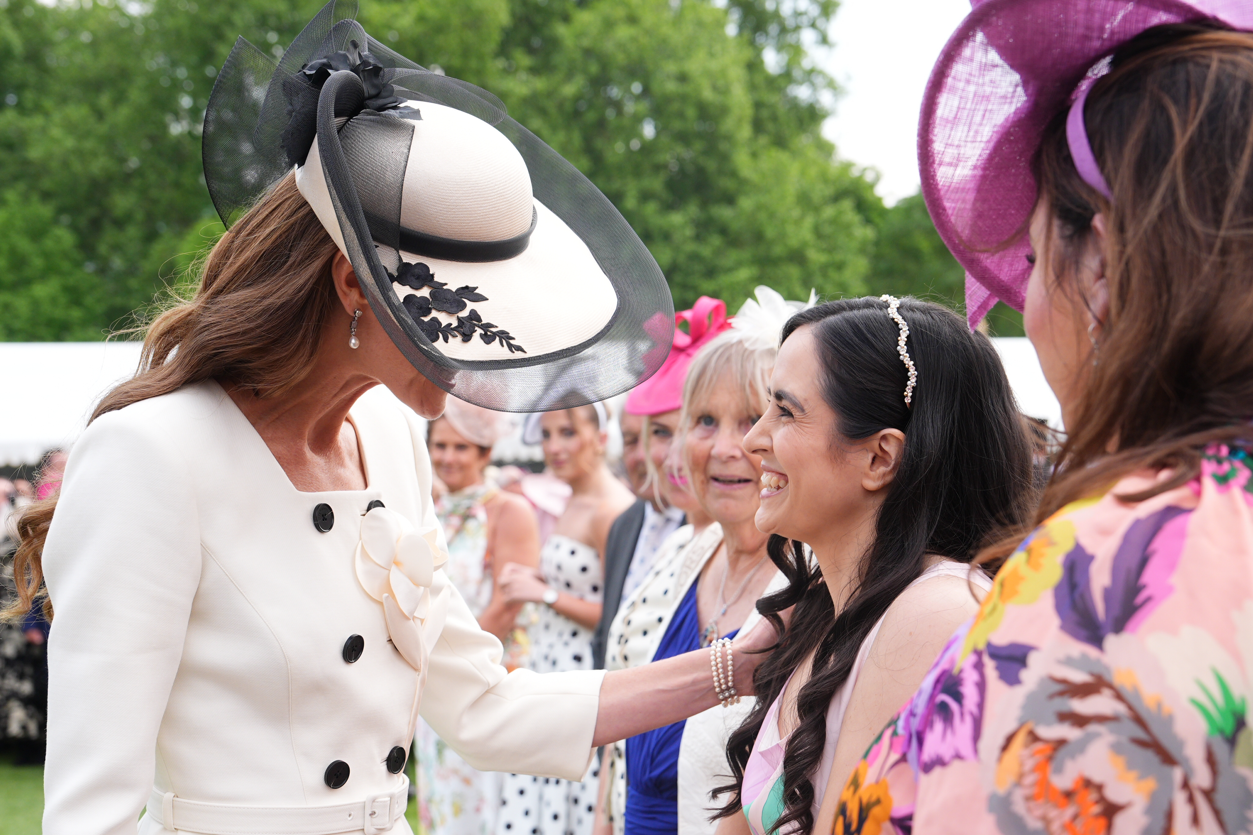 Princess Kate wearing a white and black hat touching a woman's arm