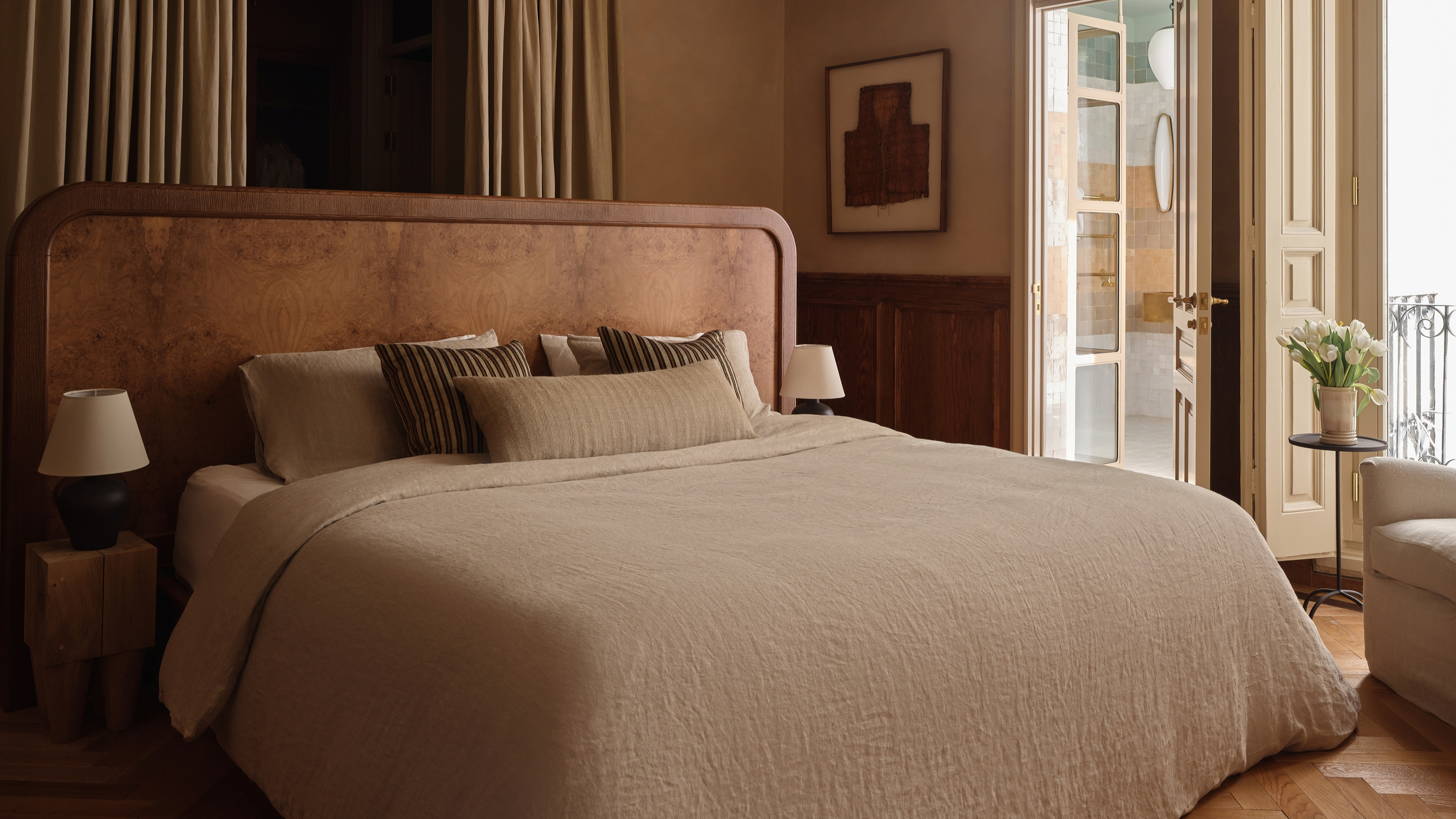 A burl bed in the center of a neutral bedroom with sophisticated linen sheets 
