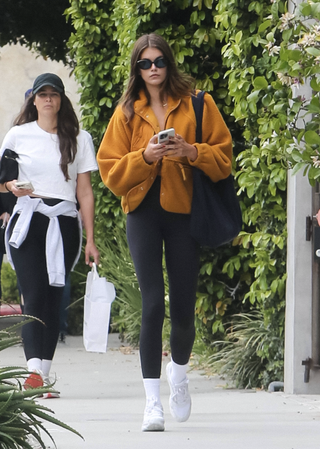 kaia gerber wears black leggings and a mustard jacket to the gym.